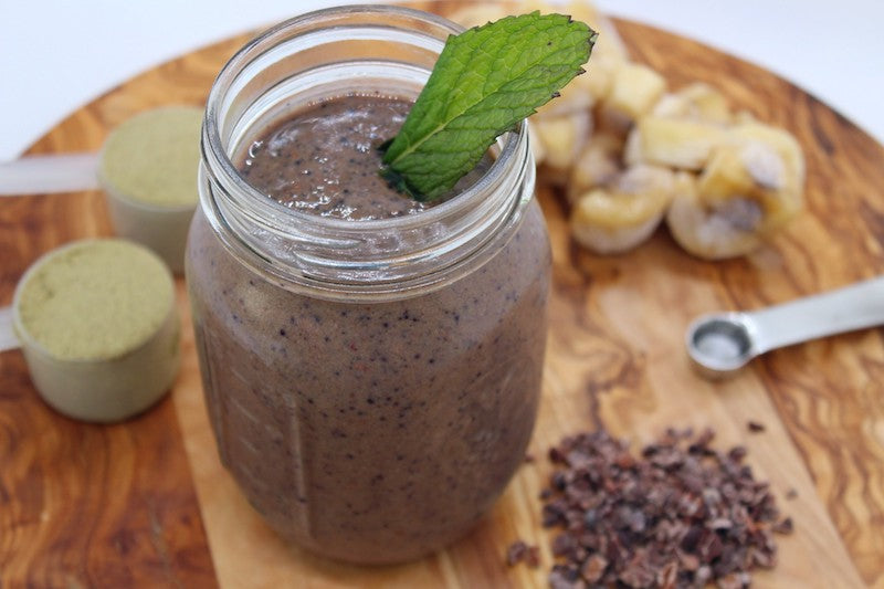 chocolate smoothie with ingredients, protein powder, banana slices, measuring spoons, cacao nibs
